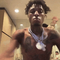 A Shirtless Man With A Necklace Around His Neck Stands In Front Of A Mirror GIF