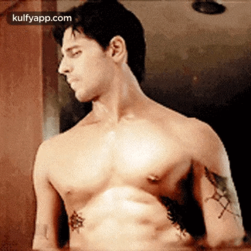 A Shirtless Man With A Tattoo On His Arm Looks At Himself In The Mirror . GIF