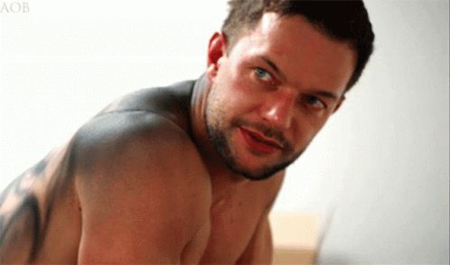 A Shirtless Man With A Tattoo On His Back Looks At The Camera With The Letters Aob Behind Him GIF