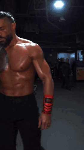 A Shirtless Man With A Tattoo On His Chest Is Wrapping His Wrist With A Red Bandage GIF