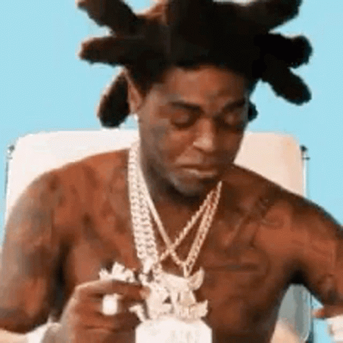 A Shirtless Man With Dreadlocks Is Sitting In A Chair Wearing A Necklace . GIF