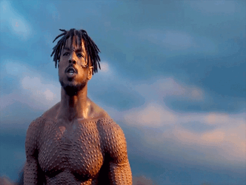 A Shirtless Man With Dreadlocks Stands In Front Of A Blue Sky GIF