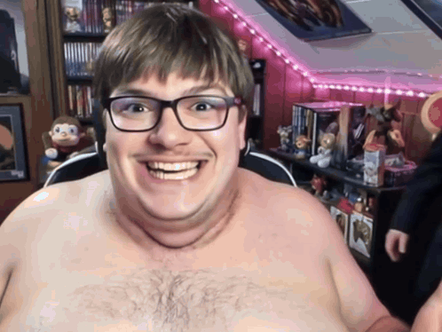 a shirtless man with glasses is smiling in a room