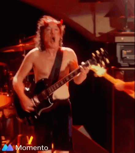 A Shirtless Man With Horns On His Head Is Playing A Guitar On Stage GIF