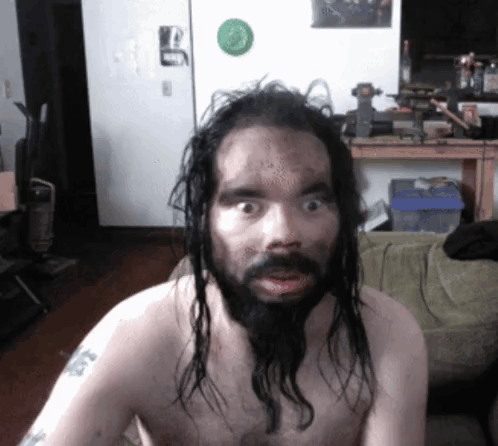 A Shirtless Man With Long Hair And A Beard Has A Tattoo On His Arm That Says ' A ' On It GIF