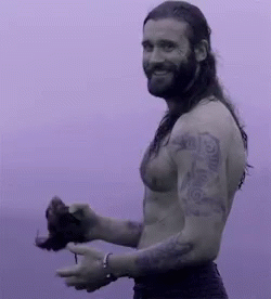 A Shirtless Man With Long Hair And A Beard Is Holding A Bird In His Hand . GIF