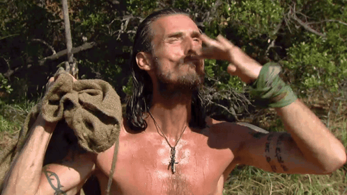A Shirtless Man With Long Hair Is Holding A Towel Over His Head GIF