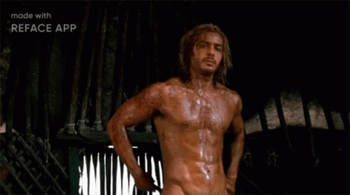 A Shirtless Man With Long Hair Is Standing In Front Of A Fence In A Dark Room . GIF