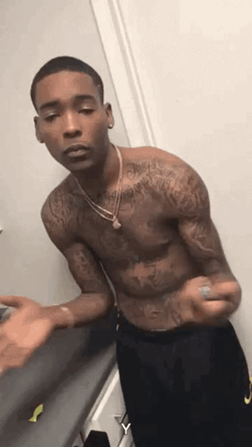 A Shirtless Man With Tattoos On His Arms And Chest Is Standing In A Room . GIF