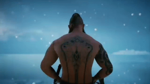 A Shirtless Man With Tattoos On His Back Is Standing In The Snow . GIF