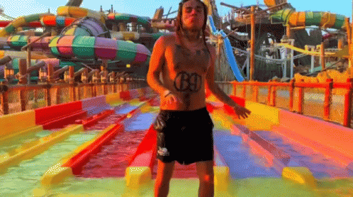 A Shirtless Man With The Number 69 On His Chest Is Standing In Front Of A Water Slide GIF