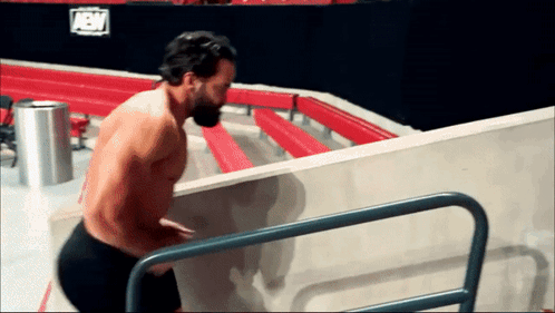 A Shirtless Wrestler Climbs Stairs In Front Of A Sign That Says Aew On It GIF