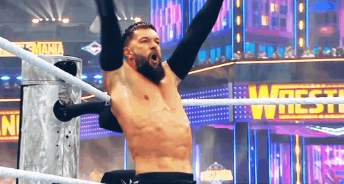 A Shirtless Wrestler Is In A Wrestling Ring With His Arms In The Air . GIF