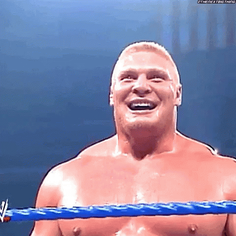 A Shirtless Wrestler Is Smiling In A Wrestling Ring With A Blue Rope . GIF