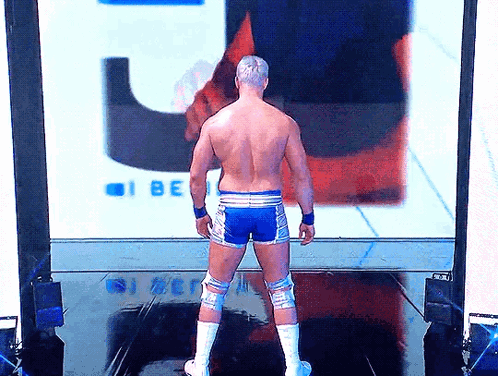A Shirtless Wrestler Is Standing In Front Of A Large Screen That Says I Be GIF