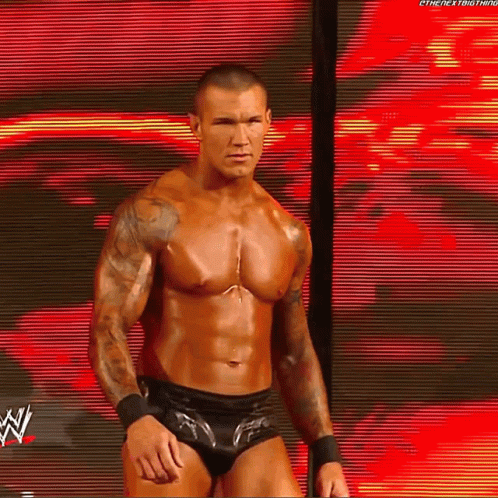 A Shirtless Wrestler Is Standing In Front Of A Large Screen With A W Logo On It GIF