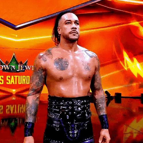 A Shirtless Wrestler Is Standing In Front Of A Sign That Says Crown Jewel Saturday GIF