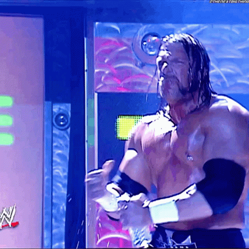 A Shirtless Wrestler Is Standing In Front Of A Sign That Says ' The Next Thing ' On It GIF
