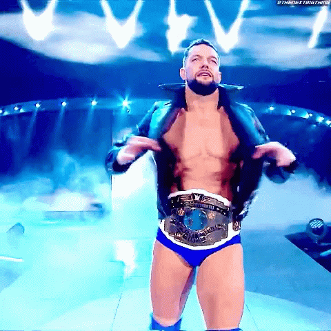 A Shirtless Wrestler Is Standing On A Stage With A Belt Around His Waist .. GIF