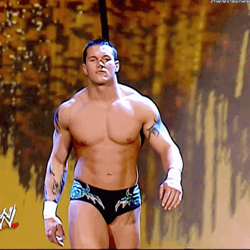 A Shirtless Wrestler Is Walking On A Stage With A W Logo In The Corner GIF