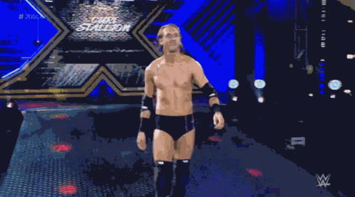 a shirtless wrestler stands in a dark room with a wwe logo in the background