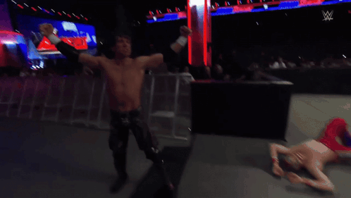 A Shirtless Wrestler Stands In A Wrestling Ring Watching Another Wrestler GIF