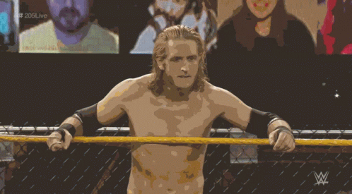 a shirtless wrestler stands in a wrestling ring with the letters w on the bottom right