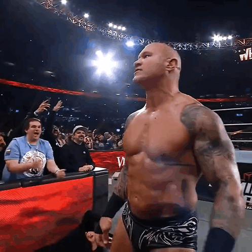 A Shirtless Wrestler Stands In Front Of A Crowd And A Sign That Says W On It GIF