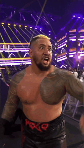 A Shirtless Wrestler Wearing A Belt With The Letter G On It Stands On A Stage GIF