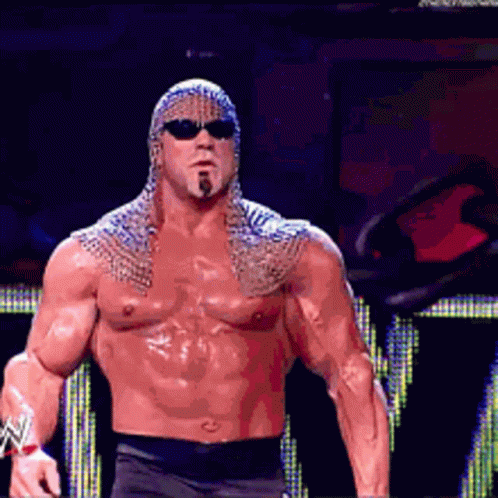 A Shirtless Wrestler Wearing Sunglasses And A Chain Mail Cape GIF