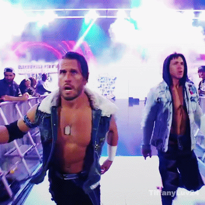 A Shirtless Wrestler With A Dog Tag On His Chest Is Walking Across A Stage GIF