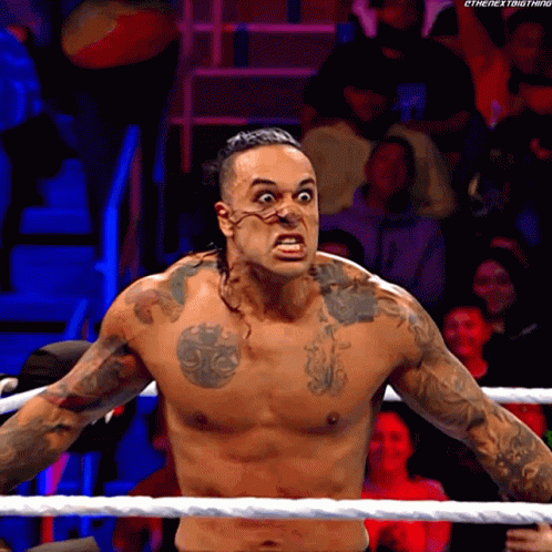 A Shirtless Wrestler With A Tattoo On His Chest Is Standing In The Ring GIF