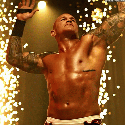 A Shirtless Wrestler With A Tattoo On His Chest Stands In Front Of Sparks GIF