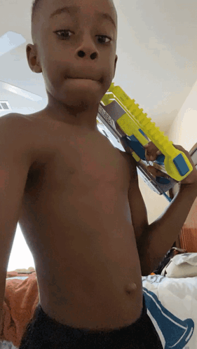 A Shirtless Young Boy Is Holding A Toy Gun GIF