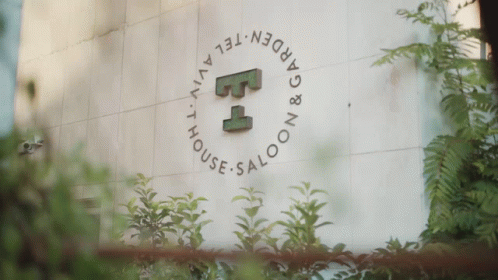 a sign for the garden tel aviv house saloon is surrounded by plants