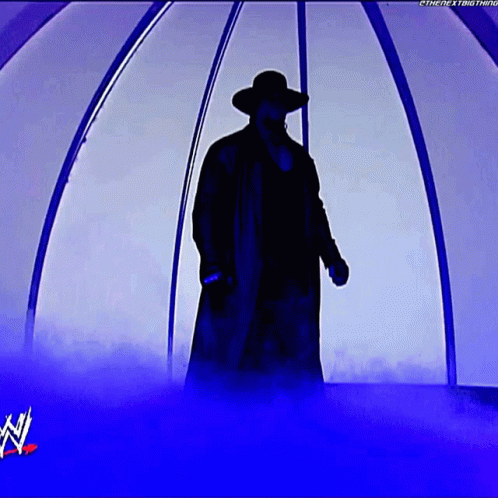 A Silhouette Of A Man In A Trench Coat And Hat Standing In A Tunnel With A W Logo In The Background GIF