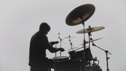 A Silhouette Of A Man Playing Drums With A White Background GIF