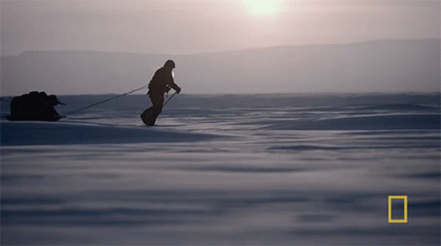 A Silhouette Of A Man Pulling A Sled In The Snow With A National Geographic Logo In The Corner GIF