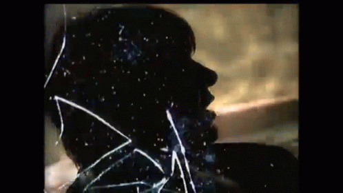 a silhouette of a man 's face is behind a broken glass .