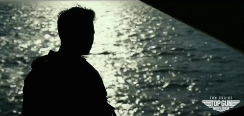A Silhouette Of A Man Standing In Front Of A Body Of Water With The Words Tom Cruise Top Gun Maverick On The Bottom GIF