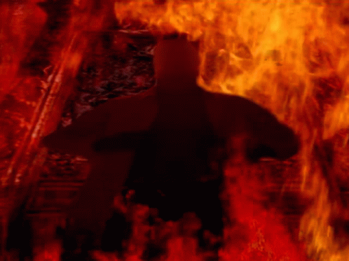 A Silhouette Of A Person In A Dark Room With Fire Behind Them GIF