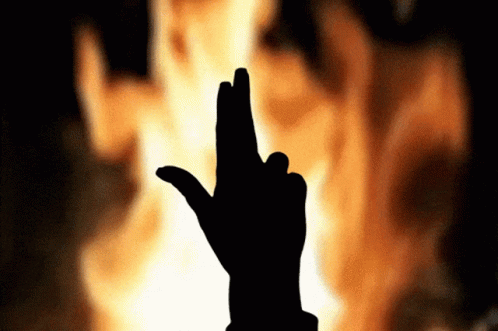 A Silhouette Of A Person 'S Hand With Their Fingers Crossed In Front Of A Fire GIF
