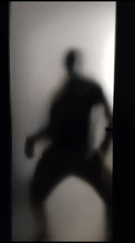 A Silhouette Of A Person Standing In A Doorway Behind A Frosted Glass Door . GIF