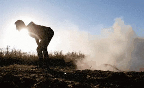 A Silhouette Of A Person Standing In A Field With Smoke Coming Out Of The Ground GIF