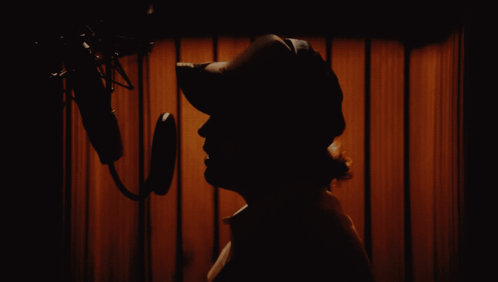 A Silhouette Of A Person Standing In Front Of A Microphone GIF