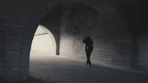 A Silhouette Of A Person Walking Through A Tunnel With Arches GIF