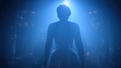 A Silhouette Of A Woman In A Blue Dress Is Standing In A Dark Room . GIF