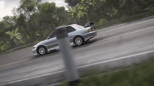 A Silver Car Is Driving Down A Road With Trees In The Background . GIF