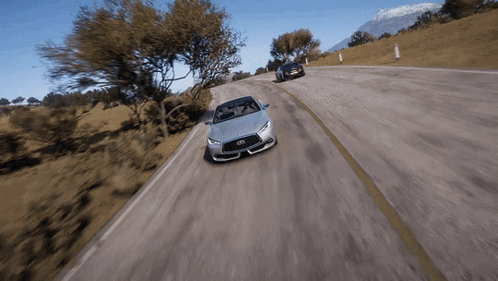 A Silver Infiniti Sports Car Is Driving Down A Road GIF