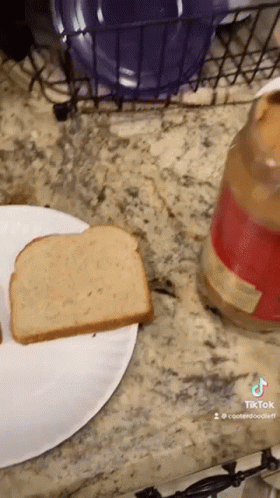 A Slice Of Bread On A Paper Plate Next To A Jar Of Peanut Butter GIF